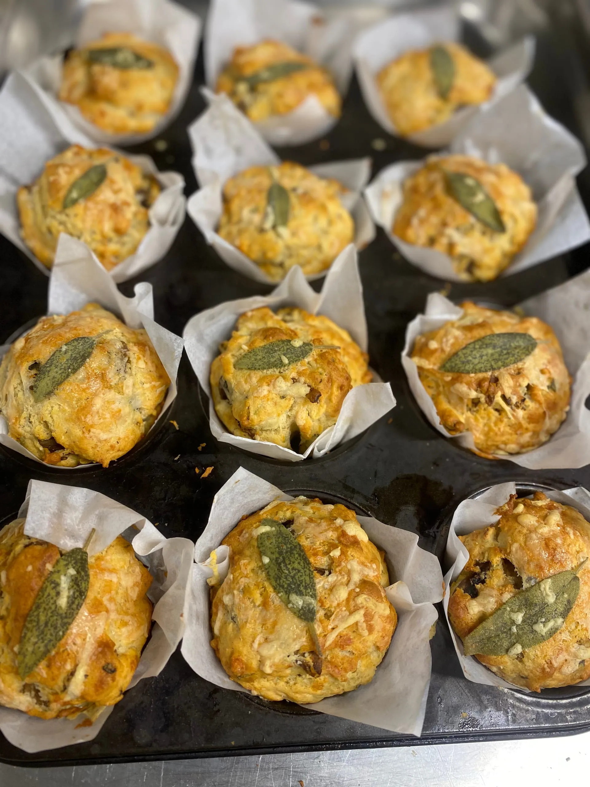 Cheese and sage muffins in their tin, a sage leaf baked onto each one